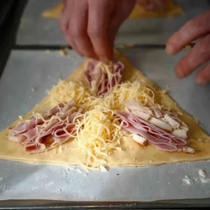 Étape 4 croissants au jambon : triangle de pâte feuilletée garni de jambon, morceaux de poulet rôti et fromage gruyère râpé