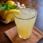 Boisson au gingembre et citron énergisante dans un verre transparent avec couleur dorée ambrée, tranche de citron et gingembre frais en garnisure