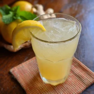 Boisson au gingembre et citron énergisante dans un verre transparent avec couleur dorée ambrée, tranche de citron et gingembre frais en garnisure
