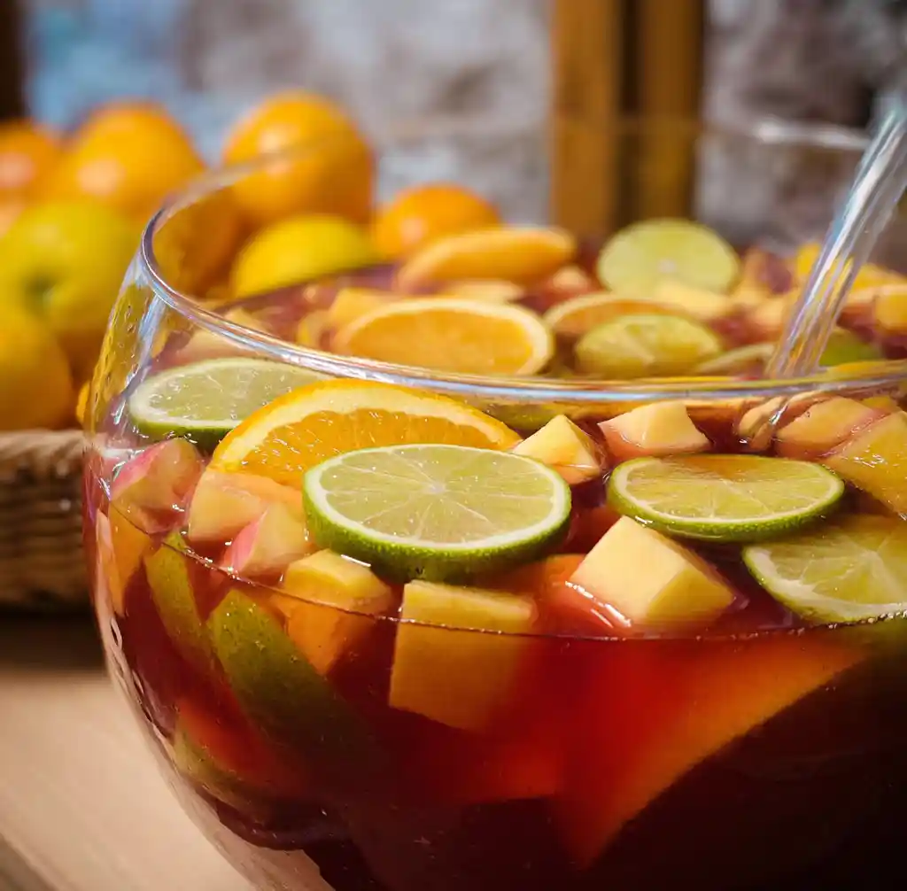 Punch sans alcool coloré aux fruits frais dans un grand saladier en verre avec ananas, oranges et citrons verts, recette de Chef Benoît
