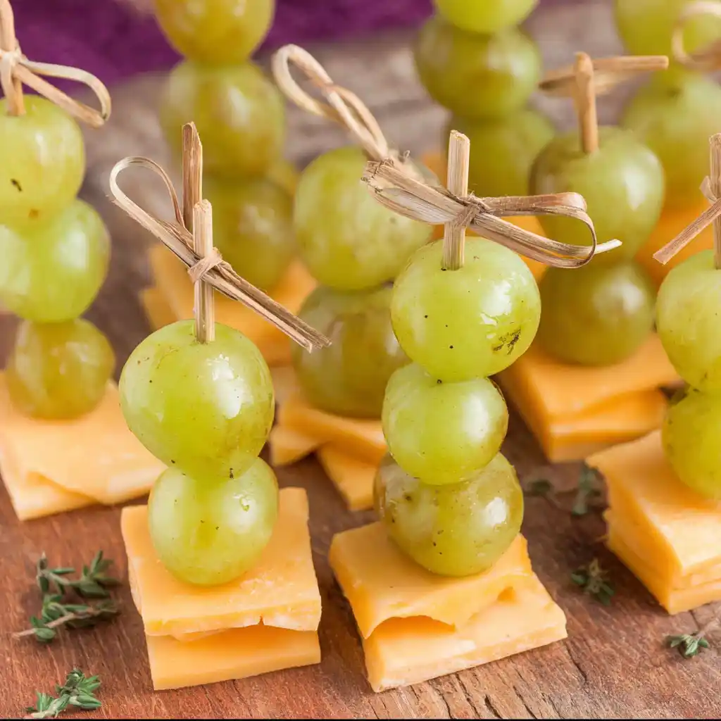 Brochettes apéritives mimolette-raisin disposées sur plateau d'ardoise avec feuilles de menthe fraîche