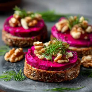 Toasts betterave et noix apéritifs disposés sur une ardoise noire avec garniture d'aneth