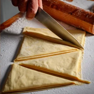 Étape 1 de la recette croissant pate feuilletée : découpe de la pâte en 16 triangles réguliers sur plan de travail blanc